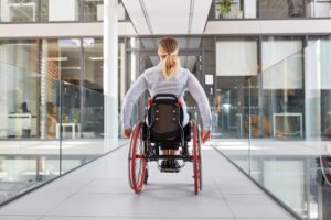 Gelähmte Frau im Rollstuhl unterwegs im behindertengerechten Bürohaus