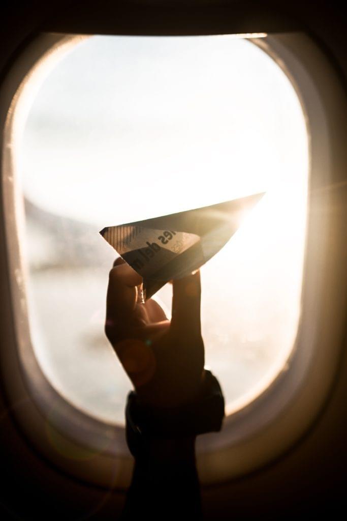 Papierflieger in Hand in Flugzeug am Fenster mit Gegenlicht