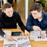 Mann in schwarzem Hemd zeigt Mann mit dunkelblauem Hemd Artikel aus einem Katalog