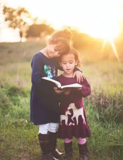 Kinder auf Wiese mit Buch in der Hand